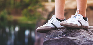 Sportowe skarpety męskie: zbliżenie na nogi młodego mężczyzny, który stoi na skale i ma na sobie białe sneakersy i czarne skarpety krótkie.